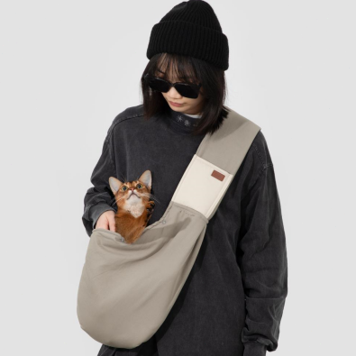 Person holding a cat in a beige sling bag against a white background