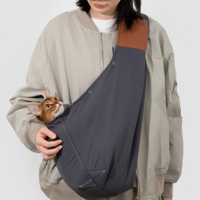 Person holding a cat in a sling with a beige cap and light gray jacket on a white background